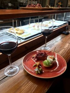 How to Choose Wine at a Restaurant: Two glasses of red wine paired with pintxos on a wooden counter at El Pintxo de Petritxol, offering a classic dining experience